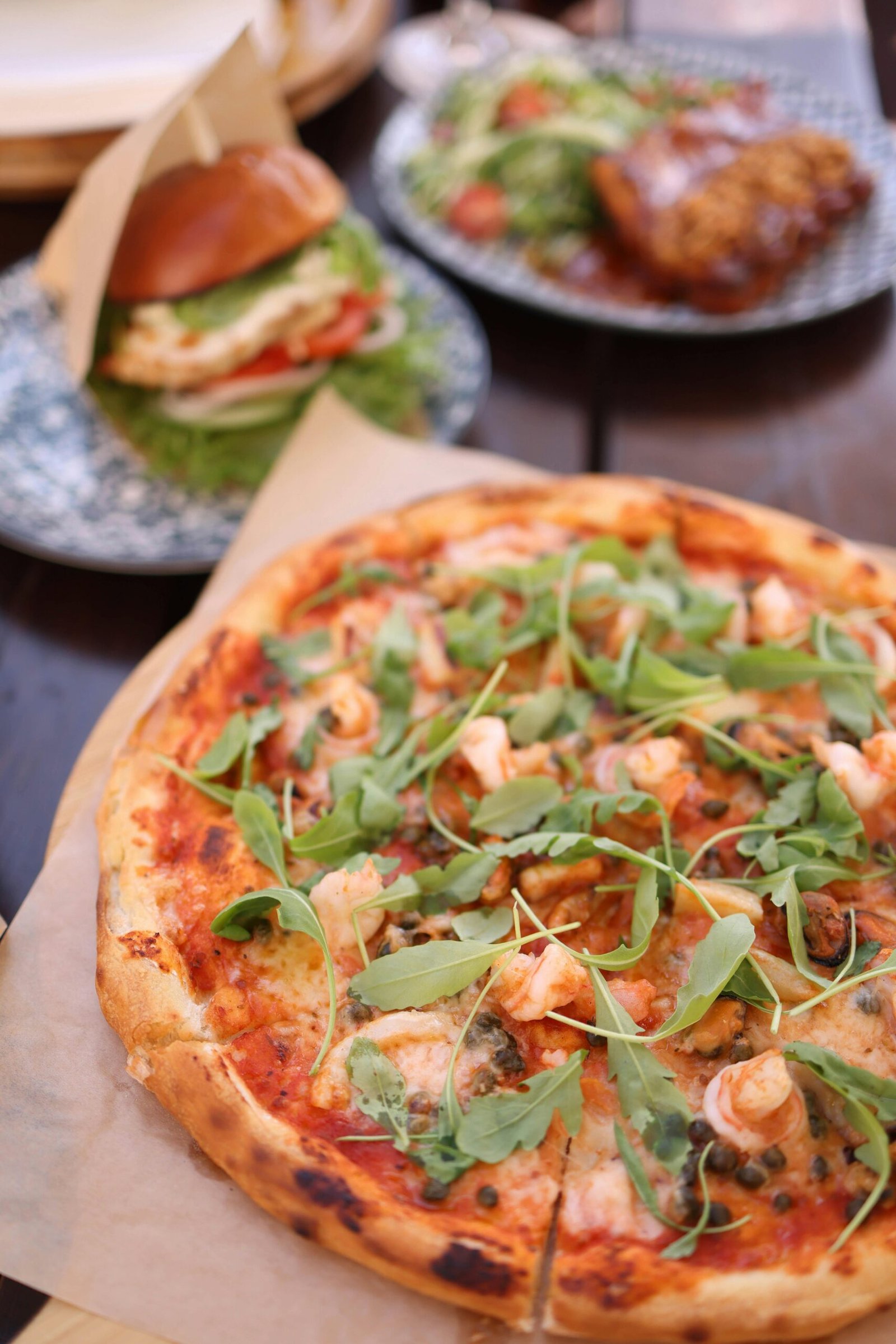 A delicious gourmet pizza topped with fresh greens alongside an appetizing burger, perfect for a hearty meal.