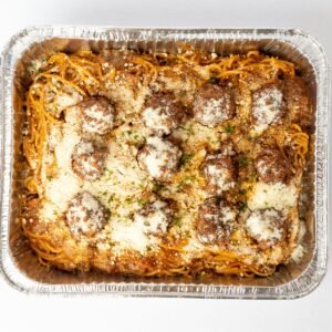 A mouth-watering view of spaghetti and meatballs topped with cheese in an aluminum tray, perfect for a tasty meal.